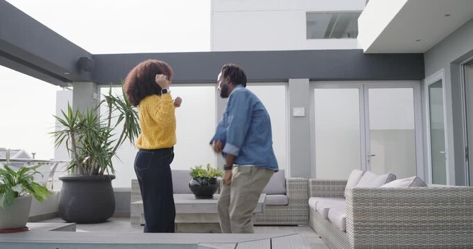 African American couple holding hands near plunge pool on rooftop breaking hold and dancing in sync