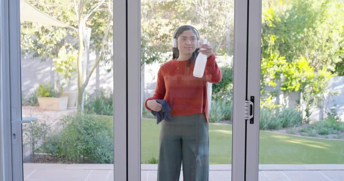 African American woman arriving patio, using spray and cloth cleaning glass door, clearing smudges