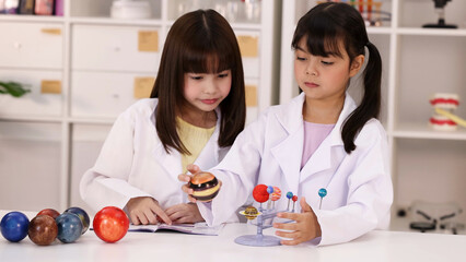 Two Young Asian Girls in Lab Coats Studying Solar System Model © blueringmedia