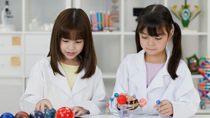 Two Elementary School Girls in Lab Coats Studying Solar System Models © blueringmedia