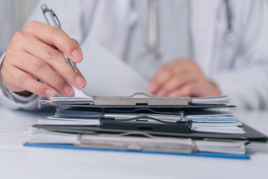 Healthcare professional reviewing stacked paperwork with pen for medical documentation records management and administrative workflow