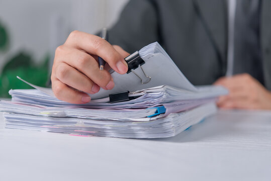 Office workers review and sort thick stacks of paperwork management with checking files with a pen at a desk. Business workflow with office worker sorting documents records.