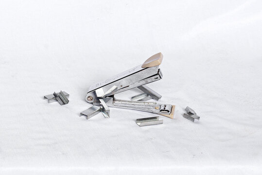 Metallic office stapler surrounded by staple refills isolated on white background