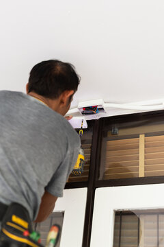 Electrician using an electric screwdriver to attach the cover of an electrical junction box.