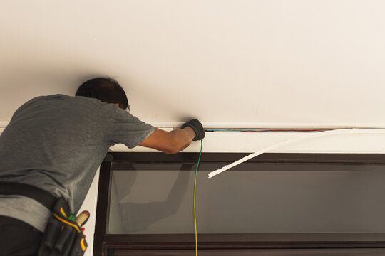 Electrician wearing protective gloves running electrical cables through ceiling.