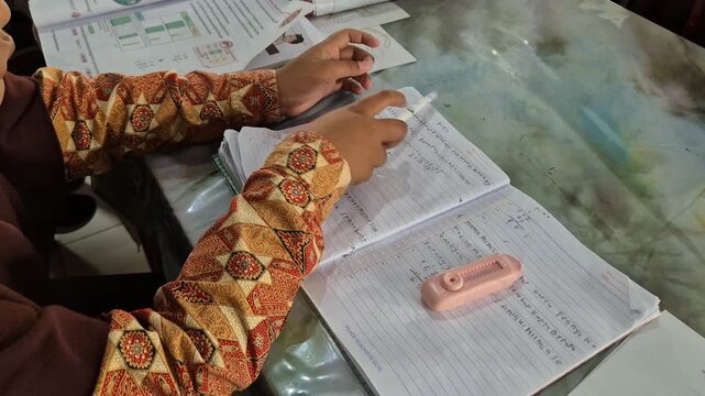 Close-up of a student in a batik uniform writing in a notebook with a pen at a desk