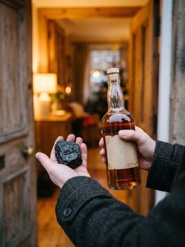 Person holding a bottle of amber liquid and rock at a wooden door  