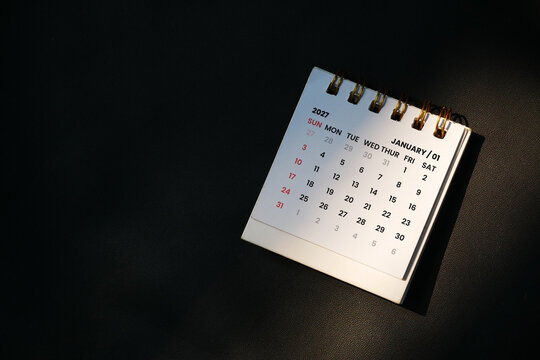 White spiral desk calendar showing January 2027 on a dark surface with dramatic lighting, representing time management and future planning concept