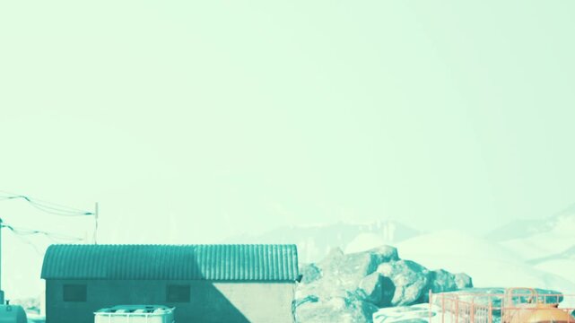 Industrial facility stands near snowy mountains with buildings and round containers outdoors during daytime