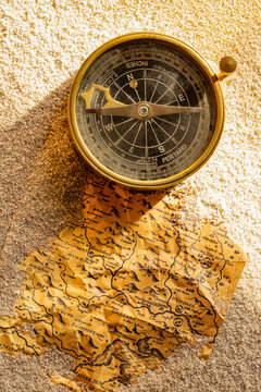 Vintage brass compass and old map partly buried in sand in sunlight background backdrop