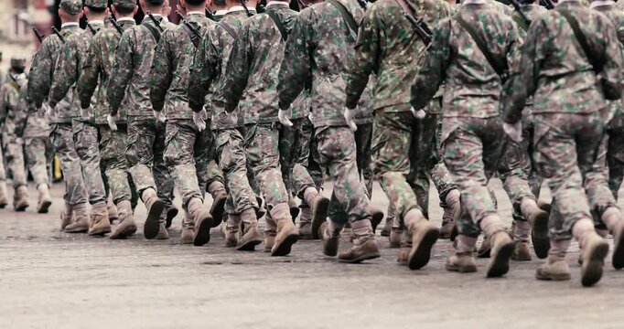 Romanian army soldiers march during a military ceremony on a rainy day.