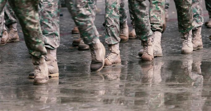 Romanian army soldiers march during a military ceremony on a rainy day.