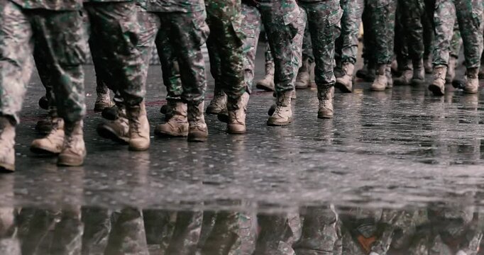 Romanian army soldiers march during a military ceremony on a rainy day.