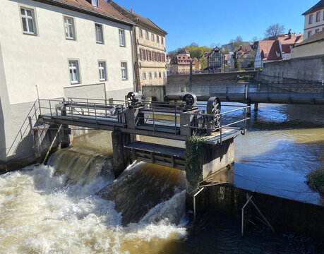 Historic water wheel weir on Regnitz River with pedestrian bridge and half-timbered buildings, Bamberg, Bavaria, Germany