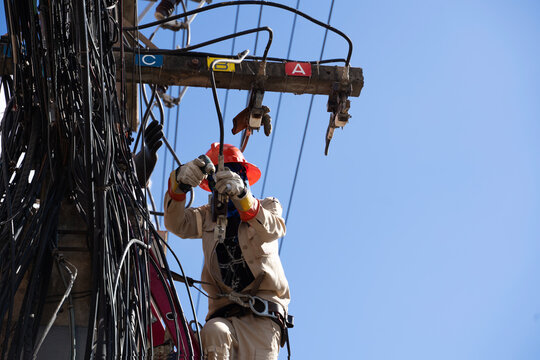 Electrical lineman using power tool on high voltage cable pole clear sky