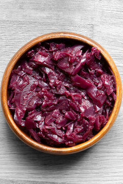 Red cabbage, braised in red wine with apple, in a brown wood bowl background backdrop. On a wooden chopping board.