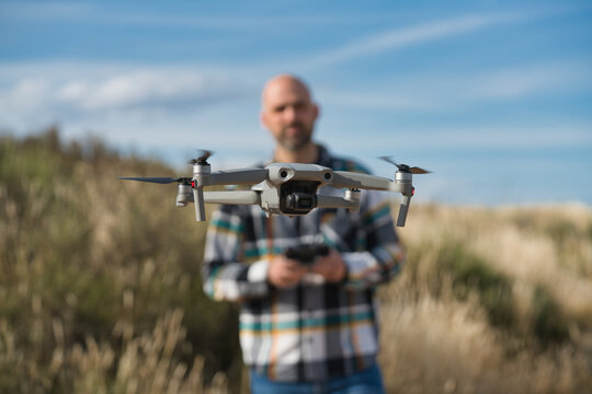 Drone hovering in focus with pilot controlling it outdoors