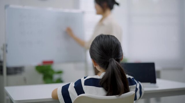 Student raising hand to ask question during classroom lesson with teacher in background and modern learning environment