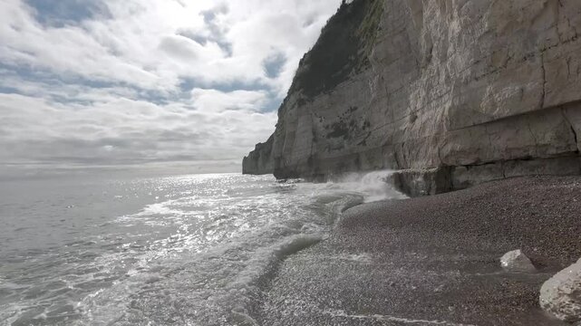 Drone flight beside white coastal cliffs and waves on a shingle beach in England