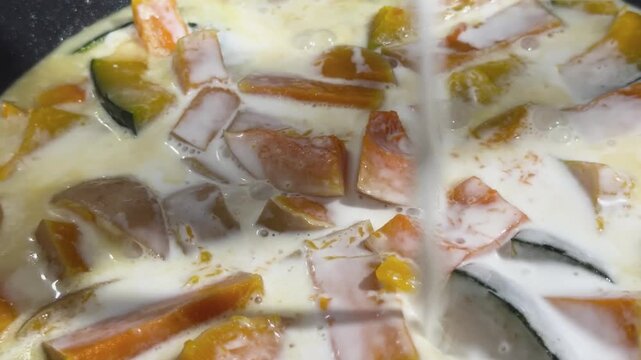 Pouring fresh coconut milk over sliced pumpkin while cooking traditional Thai sweet dessert in a hot pot 4k video close up shot