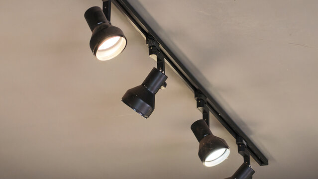 Track lighting fixture with black adjustable spotlight illuminating indoor ceiling, creating modern architectural atmosphere for retail or residential space