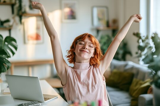 Young woman with red hair stretching at her workspace, smiling with eyes closed, enjoying a peaceful break in her bright home office setting