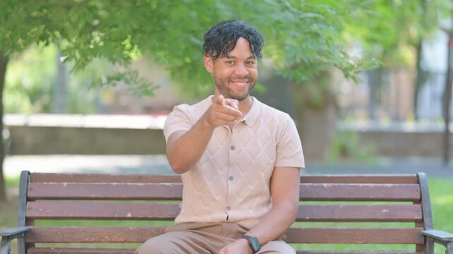 Mixed Race Man on Bench Pointing at Camera Outdoor