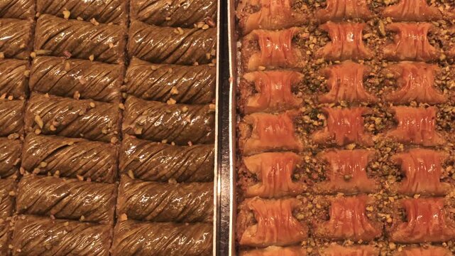 Baklava pastries sit in metal trays at a sweet shop in Istanbul, Turkey, with rows of syrup-coated rolls and nut-filled pieces on display.