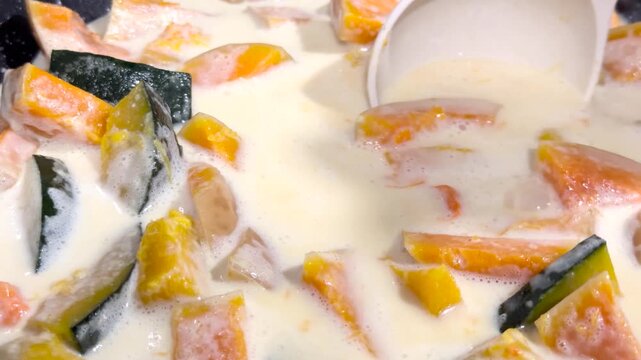 Stirring traditional Thai sweet pumpkin dessert with a ladle in hot coconut milk soup 4k video close up