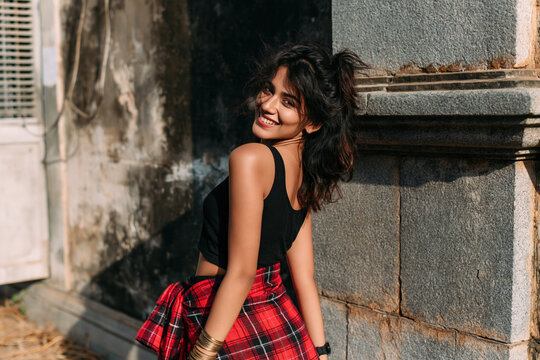 Indian girl in 90s-style grunge clothing stands on the street during the day.