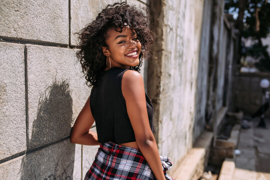 An African American girl in 90s-style grunge clothing stands on the street during the day.