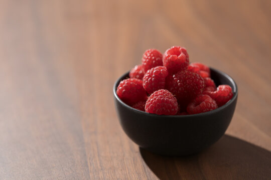 Bowl of fresh raspberries on walnut wood table with copy space
