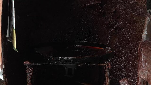 Cinematic close-up footage of a gloved artisan hand dipping a traditional copper batik cap stamp into a hot wax pan in a dark batik workshop. Authentic Indonesian wax printing process.