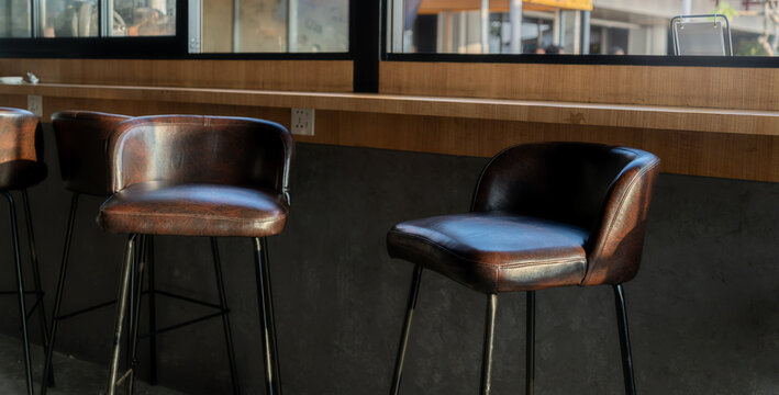close up of elegant brown leather bar stools with thin metal legs arranged neatly at a long wooden counter in a contemporary cafe or restaurant.
