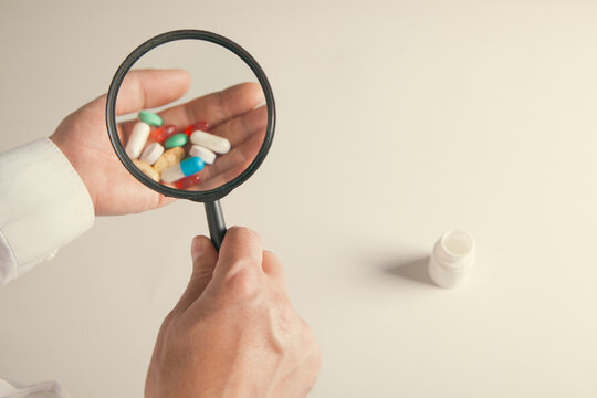 Close-up of a man holding a magnifying glass of pills