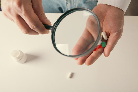 Close-up of a man holding a magnifying glass of pills