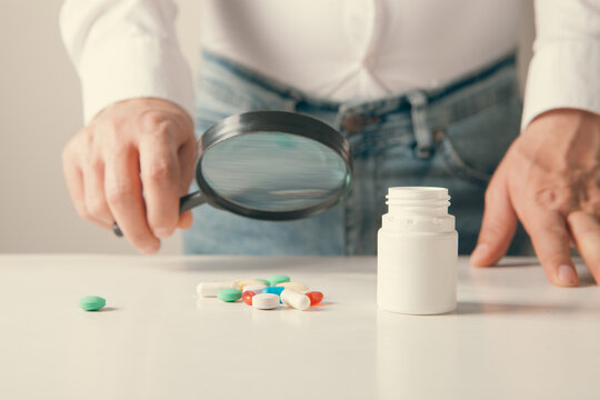Close-up of a man holding a magnifying glass of pills