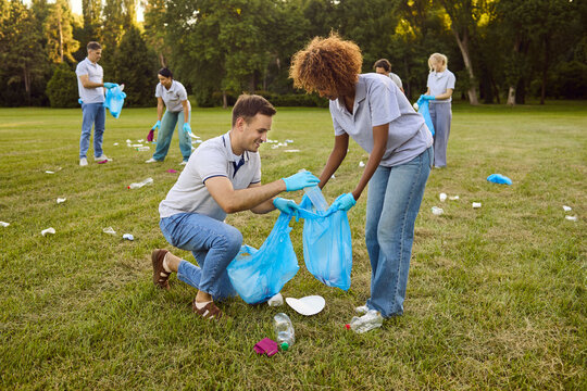 Volunteers cleanup park litter with gloves and teamwork. A group collects trash into blue bags, promoting recycling for the local environment. Symbol of community sustainability action.