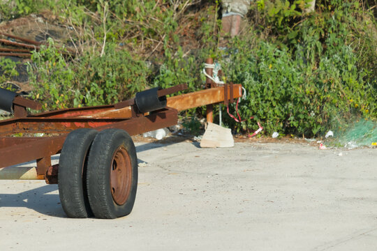 Old Rusty Boat Trailer with Dual Wheels Parked on Concrete Next to Overgrown Vegetation