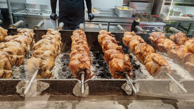 Whole grilled chickens roasting on charcoal rotisserie spits in a restaurant kitchen