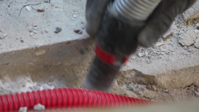 Pneumatic demolition hammer chipping hard concrete surface near flexible red protective conduit during construction. Close up shot.
