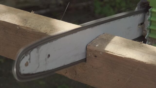 Close-up of a chainsaw cutting through a rough wooden beam on a sunny day.