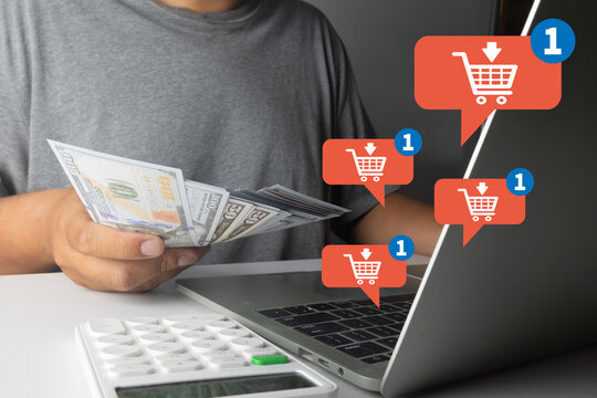 Man holding US dollar bills with a laptop and calculator. Digital overlay of red shopping cart notification icons. Concept of online shopping, e-commerce, consumerism, and digital retail.