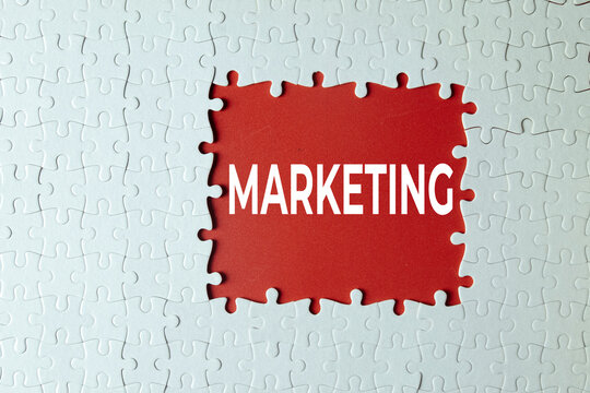 White jigsaw puzzle with a missing center section revealing a red background with the word MARKETING. Concept of business strategy, advertising plan, finding the missing piece, and solution.