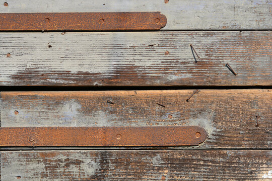This detailed close up background texture highlights aged grey wooden planks with peeling paint rusty iron hinges and several old bent nails.