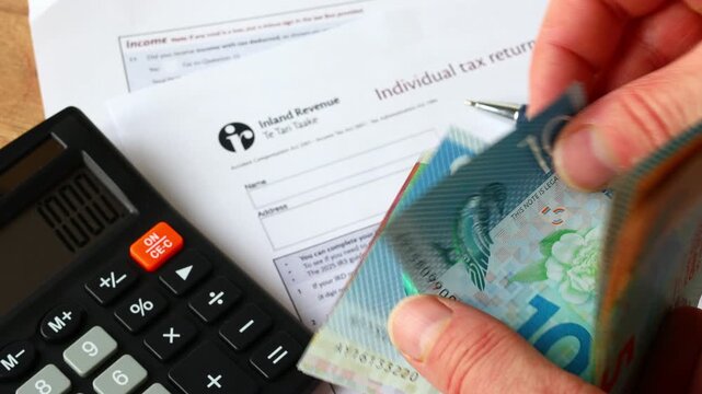 New Zealand individual tax return. A person working with New Zealand dollars, a tax form, and a calculator. Financial and business concept.
