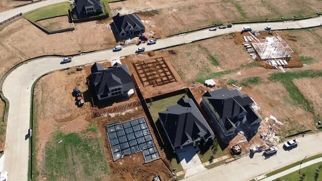 Concrete loading aprons border perimeter fence line Denton County sectors along DFW Metroplex. Compacted earth pads neighbor partially framed houses, modern shingle roofs, Flower Mound, Texas
