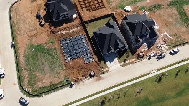 Framed home structures rise prominently within DFW Metroplex along North Texas Region. Dark composite rooftops border leveled red soil pads, concrete curbs, newly, Flower Mound, Texas