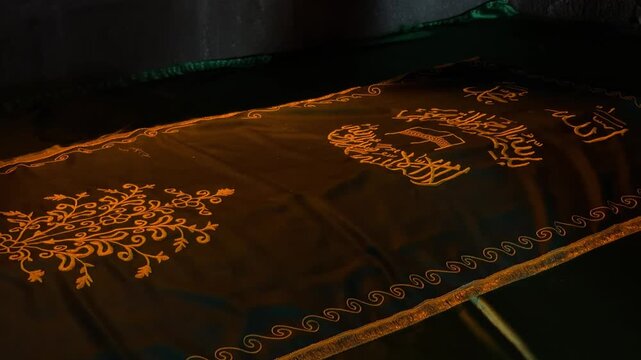 Erzurum, Turkey - September 25, 2026: Ornate black fabric with golden floral embroidery and Arabic calligraphy, slowly revealing detailed decorative patterns in dim light