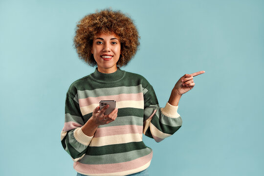 Smiling woman with phone pointing to copy space.